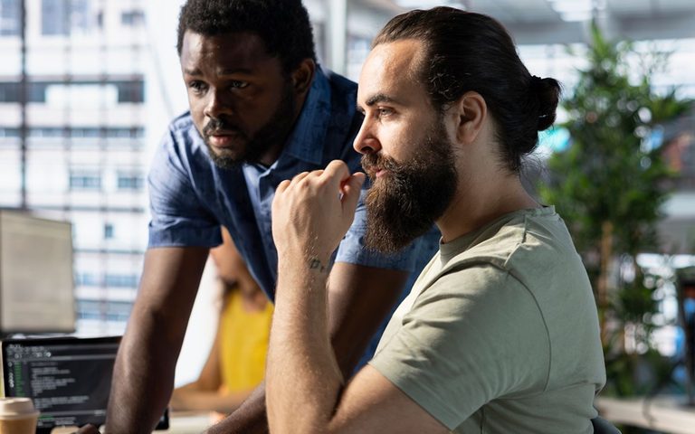 Two colleagues at a screen, one considering a decision.