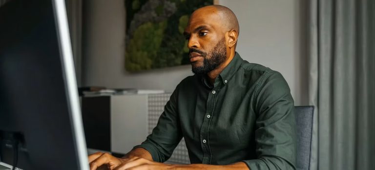 A developer at a desktop in a warm, plant-filled office, focused and thinking.